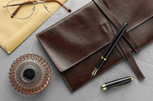 Flat lay composition with stylish fountain pen and inkwell on light grey textured table