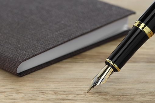 Stylish fountain pen and notebook on wooden table, closeup