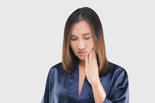 A woman in a dark blue satin robe has a toothache.
