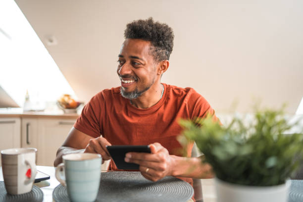 cheerful black male using an e-reader at home - e reader cheerful indoors lifestyles fotografías e imágenes de stock