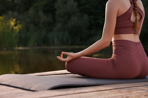 Woman practicing Padmasana on yoga mat on wooden pier near pond, closeup with space for text. Lotus pose