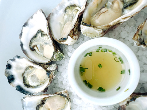 Horizontal high angle closeup photo of Australian natural oysters in the half shell on rock salt with a small white bowl of champagne and chive dipping sauce.