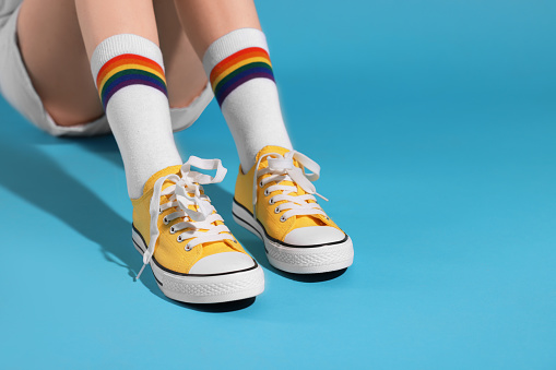 Woman wearing yellow classic old school sneakers on light blue background, closeup. Space for text