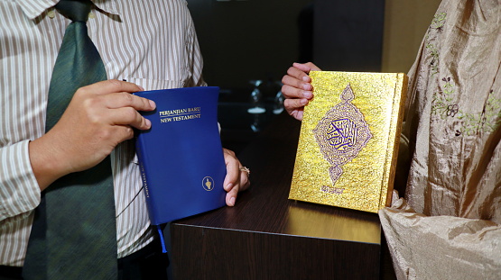 holding the bible of the new testament and the book of the quran
