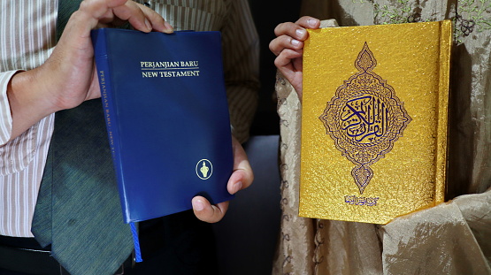 holding the bible of the new testament and the book of the quran