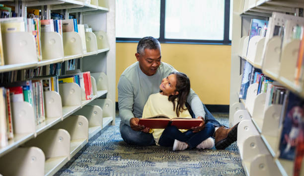 asian father, multiracial daughter, reading in library - looking over shoulder looking men looking up foto e immagini stock