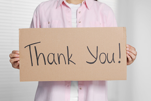 Woman holding cardboard sheet with phrase Thank You indoors, closeup