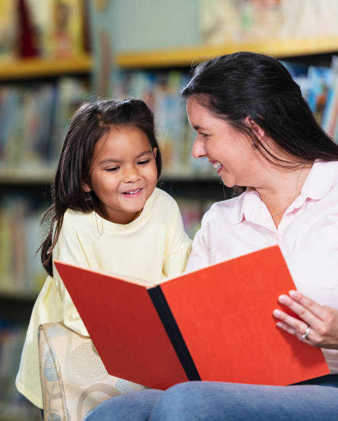 istock Mother and multiracial daughter, reading in library 1913333761
