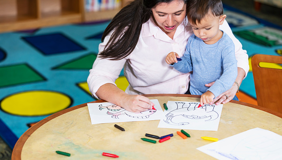 A mother with her toddler sitting at a table color pictures with crayons. The boy is multiracial, Asian and White, 19 months old.