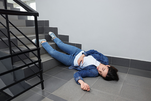 Unconscious woman lying on floor after falling down stairs indoors