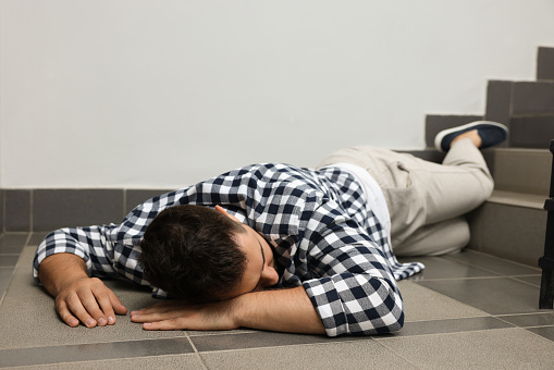 Unconscious man lying on floor after falling down stairs indoors