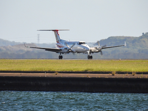 A Beech King Air 350C plane, registration VH-AMQ, of the NSW Air Ambulance landing on the third runway of Sydney Kingsford-Smith Airport as flight AM288 from Tamworth.  This image was taken from Mill Stream Lookout, Botany Bay, on a sunny afternoon on 6 January 2024.