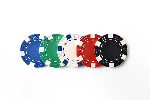 Casino background with detail of five different colored plastic chips in a row on white isolated background. Top view.