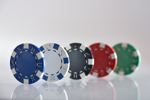 Detail of five different colored plastic gambling game chips in line on white isolated background. Front view.