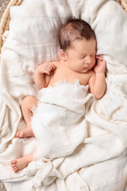istock Cute newborn baby sleeping on white blanket in wicker crib, top view 1913394918
