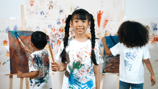 istock Creative girl pose at camera while diverse children painting behind. Erudition. 1913419295