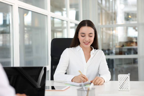 istock Happy woman taking notes at white desk in open plan office, space for text 1913457238