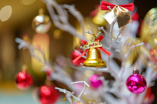 Beautiful ornamental gold bell decoration hanging on a branch on an artificial Christmas Tree. Image focuses on the star but it is surrounded by baubles and other decorations.