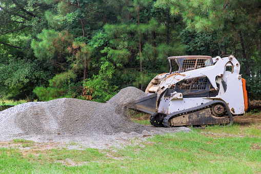 During construction, bobcat mini loader is moving bucket containing crushed stone gravel