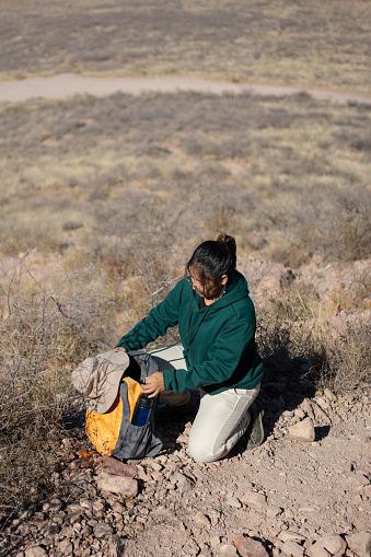 Woman on a deserted mountain arranging her backpack to go on a hiking adventure on vacation