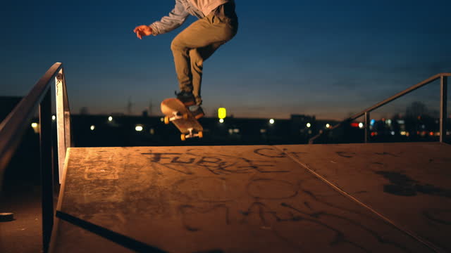 SLO MO Side View of Young Man Performing Shunts with Skateboard on Skate Park at Night