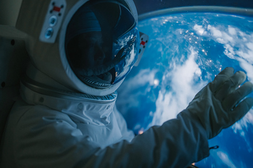 Asian chinese mid adult female astronaut looking at earth through window from spaceship at outer space