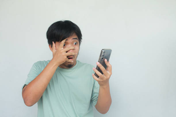 istock Young Asian man showing surprised expression while typing on his mobile phone. 1913879111