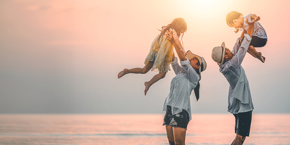 Happy asian family playing sea on the Beach at Sunset. Family enjoys carrying children around the beach. Family, travel, lifestyle and vacations, holiday concepts.