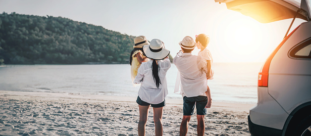 Happy family running on the beach in the sunset. Parents were holding their children and watching the sunset behind the car. Summer vacations, Holiday and travel family concept.