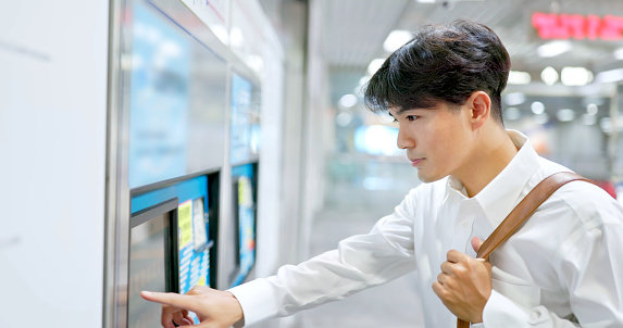 asian businessman is using ticket vending machine to buy mrt pass