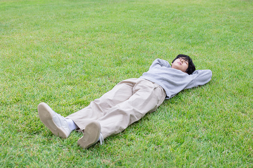 A young man lies down on a green lawn in an outdoor park on a sunny day and relaxes