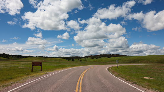 White clouds, blue sky, green prairie and a winding road in Wind Cave National Park