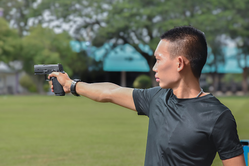 Asian young teens holding automatic black pistol in hands and ready to shoot, concept for shooting sport, robbery, safty, security, shooting training and bodygaurd.