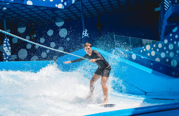 Young man surfing with trainer on a wave simulator at a water amusement park