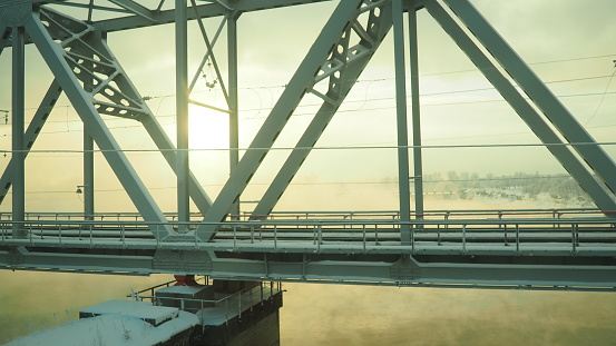 Volkhov, Russia, the railway bridge over the Volkhov River next to the hydroelectric power station. Severe frost -30 degrees Celsius. Low polar sun. Yellow cold fog