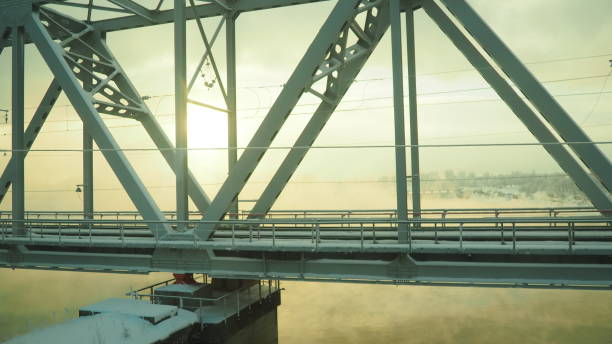 Volkhov, Russia, the railway bridge over the Volkhov River next to the hydroelectric power station. Severe frost -30 degrees Celsius. Low polar sun. Yellow cold fog stock photo