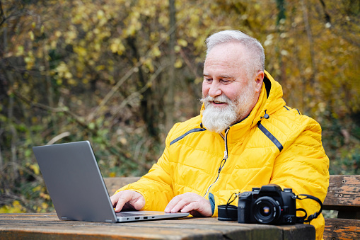 Positive photographer working on the laptop in the autumn forest