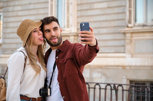 Young Caucasian couple taking a selfie stick out tongue while sightseeing the city of Madrid, Spain.