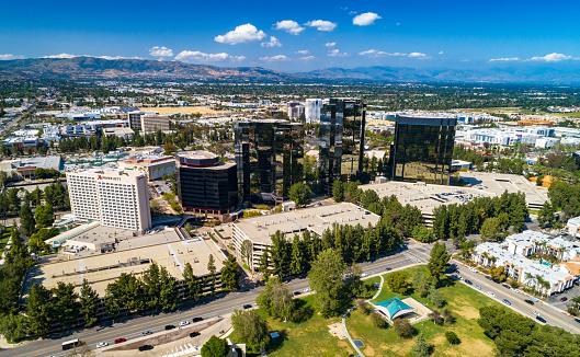Aerial of Warner Center in Woodland Hills, a neighborhood of Los Angeles, CA, with other areas of the city, mountains, and a blue sky with puffy white clouds in the distance.