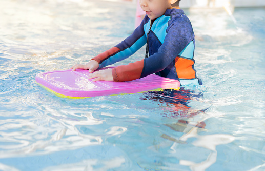 Lonely child warm up with swimming kickboard before practicing to swim in the blue swimming pools.