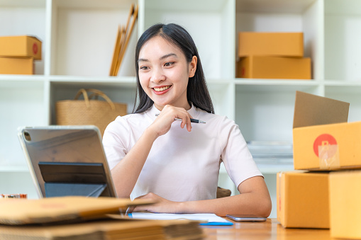 Happy young online businesswoman sitting at her desk smiling at her customer on the tablet while working at her home office