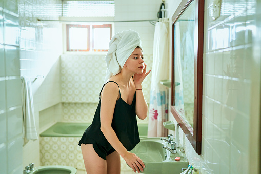 Female inspecting complexion and caring for skin in an old-fashioned bathroom setup, reflecting a routine of beauty and personal hygiene.