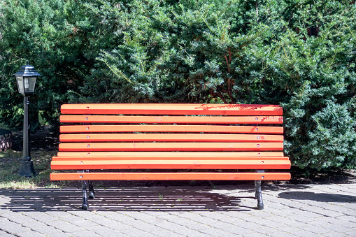 Orange wooden bench with forged metal legs in the park on a green wooden background