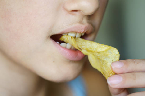 istock Crop anonymous girl biting crunchy potato chip at home 1914201100