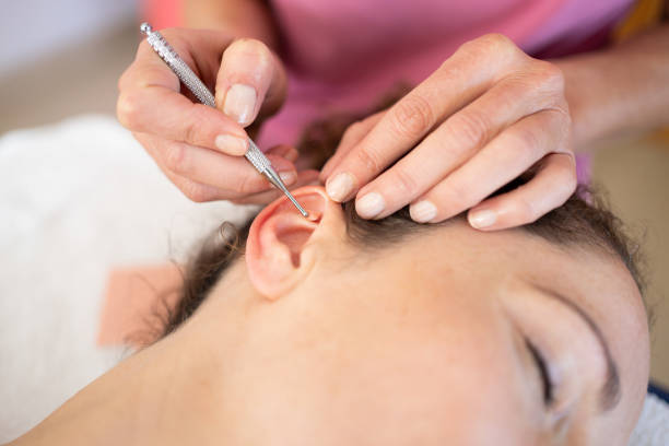 Crop chiropractor massaging ear of woman during auriculotherapy in beauty salon stock photo