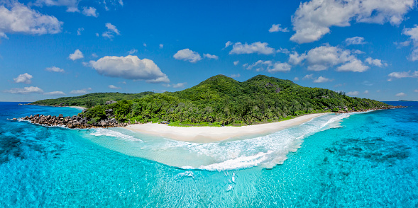 Tropical beach shot from a drone waves hitting the white sandy beach with corals rocks and lagoon - aerial series seychelles