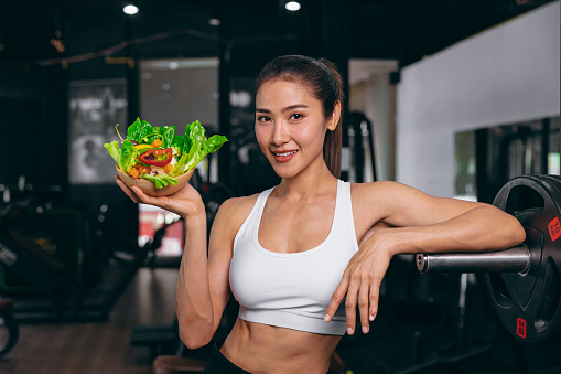 sport healthy beautiful asian woman showing vegetables mix salad for diet food low calories in fitness sport club