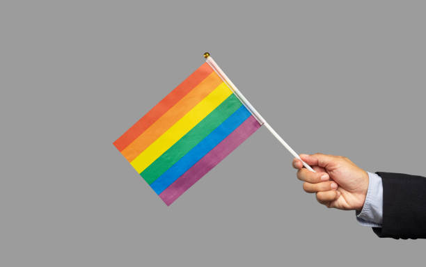 istock Close-up of a hand holding a rainbow flag while standing on a gray background. 1914262030