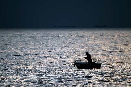 silhouette of a fisherman and his boat fishing in the sea before the storm