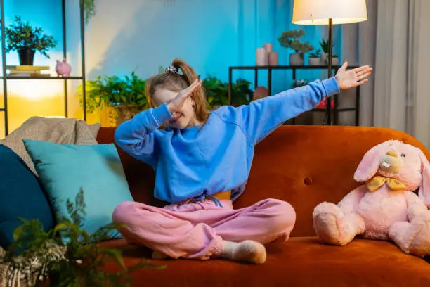 Photo of Happy toddler child girl dancing and moving to rhythm making trendy dub dance gesture at modern home